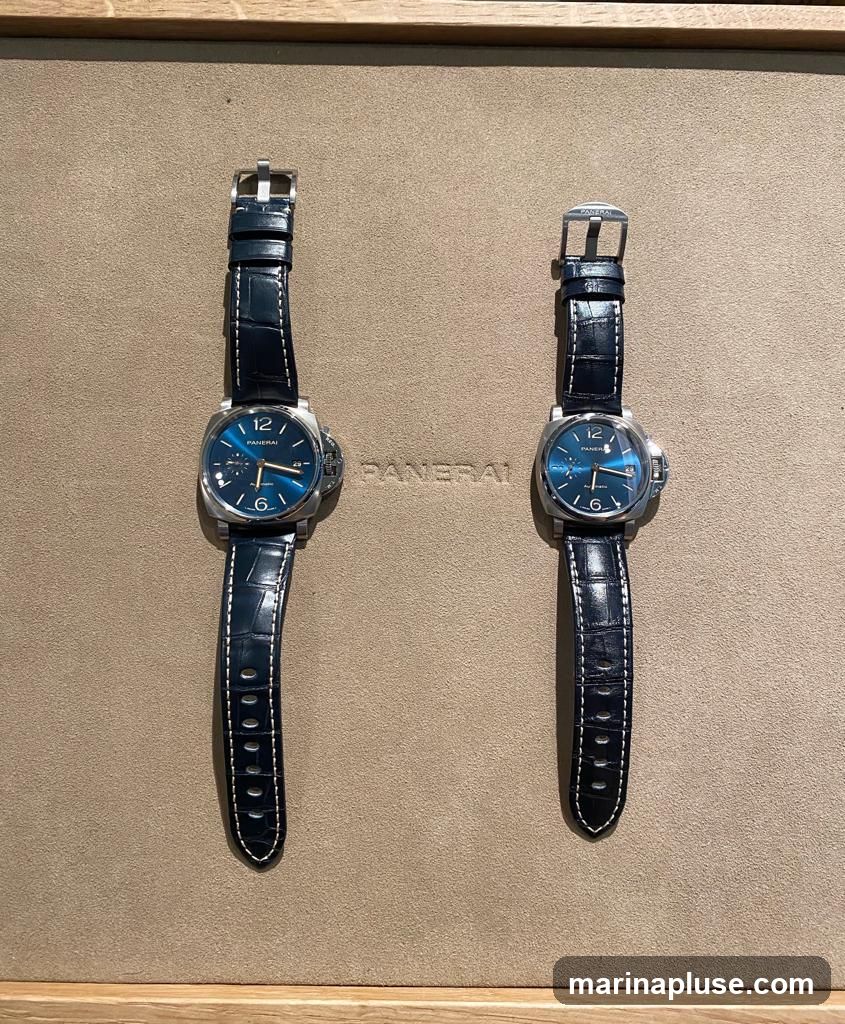 Two luxury Panerai watches with blue dials and dark blue alligator straps are displayed on a textured beige background. The brand name "PANERAI" is visible in raised lettering between the two watches.