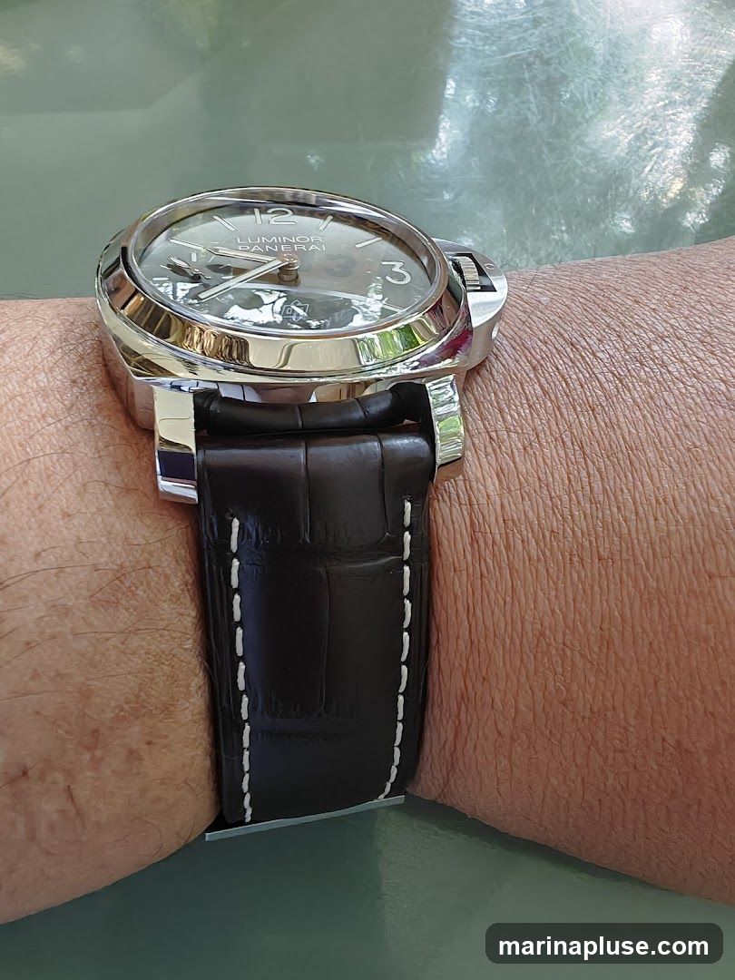 A close-up shot of a Panerai Luminor watch on a person's wrist. The watch has a dark, textured strap with white stitching and a polished metal case. The watch face is visible, showing the brand name 'LUMINOR PANERAI' and numerals.