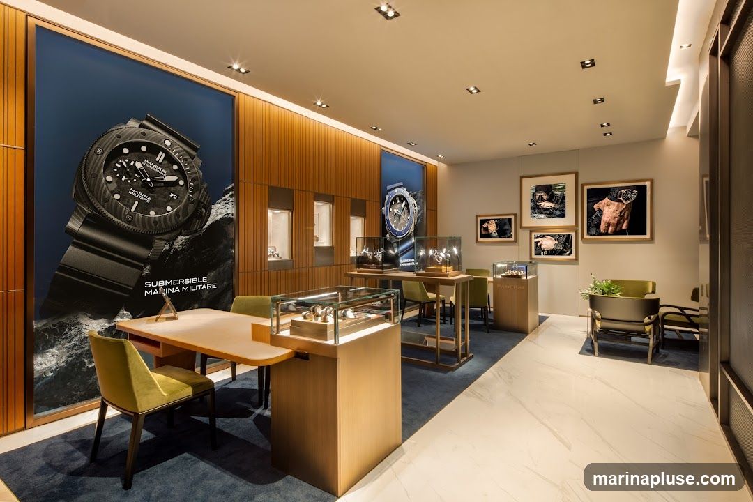 The interior of a modern watch store, featuring display cases with watches, large promotional posters of watches, and framed artwork on the walls. The store has a clean, minimalist design with wooden accents and plush seating areas.