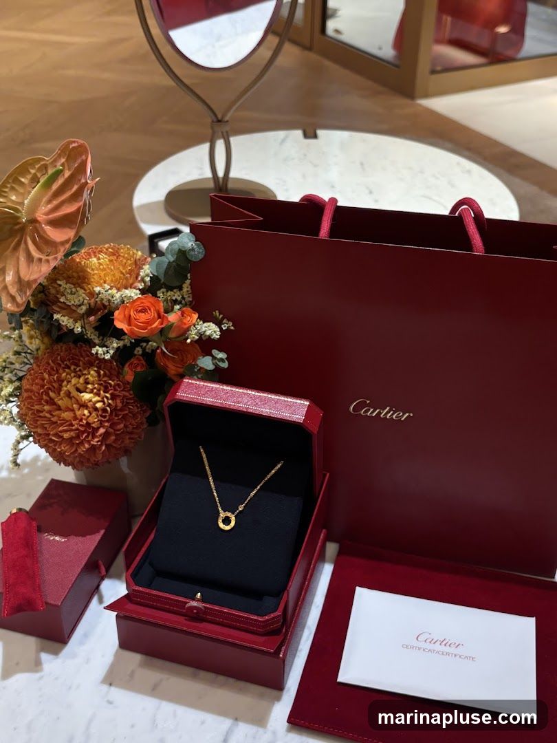 A Cartier necklace is displayed in its red jewelry box, next to a red Cartier shopping bag and a bouquet of orange and yellow flowers. A certificate from Cartier is also visible.