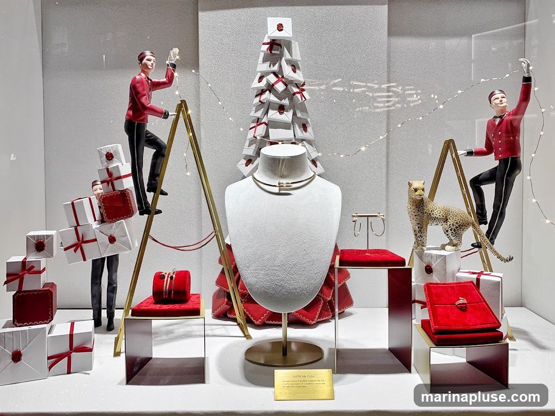 A festive window display features mannequins dressed as bellhops decorating a Christmas tree made of gift boxes. A leopard statue stands near a display of jewelry, including a necklace and earrings. The display is adorned with fairy lights and red and white gift boxes. A small plaque reads "JUSTE UN CLOU" and describes the collection.
