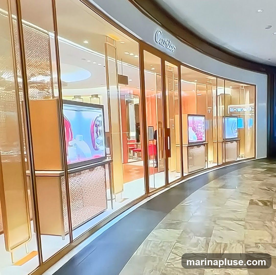 A wide shot of a luxury jewelry store's exterior. The storefront features a curved glass facade with gold-colored framing. Inside, displays showcase products, and red seating is visible. The store's name, "Cartier," is prominently displayed in script above the entrance.