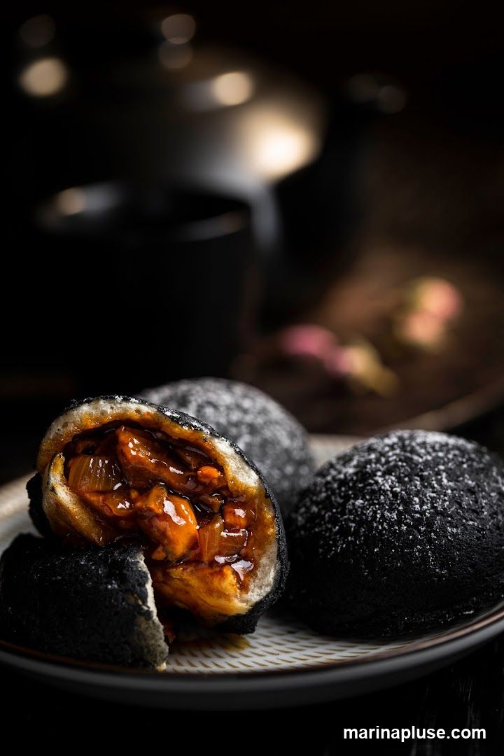 A close-up shot of three dark, round buns dusted with powdered sugar, served on a patterned plate. One bun is cut in half, revealing a rich, savory filling of meat and onions in a glossy sauce. The background is dark and blurred, with hints of bokeh lights and decorative elements.
