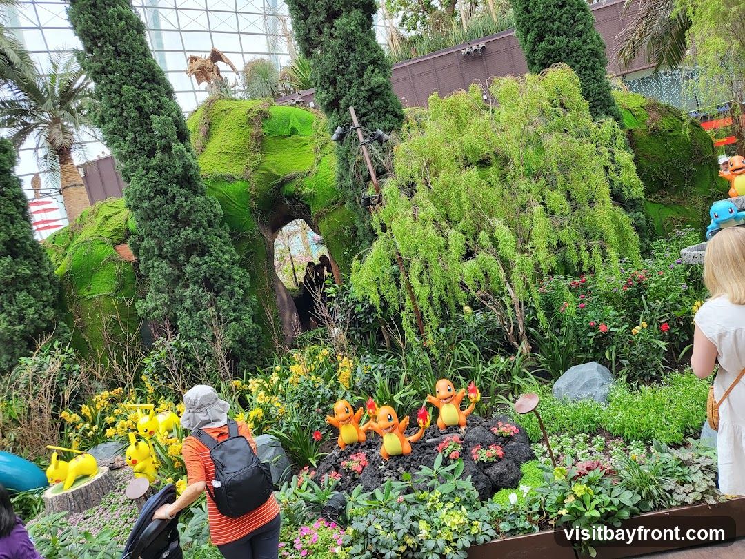 A lush garden display featuring various Pokemon characters, including Pikachu and Charmander, integrated into a moss-covered landscape with trees and flowers. People are observing the display.