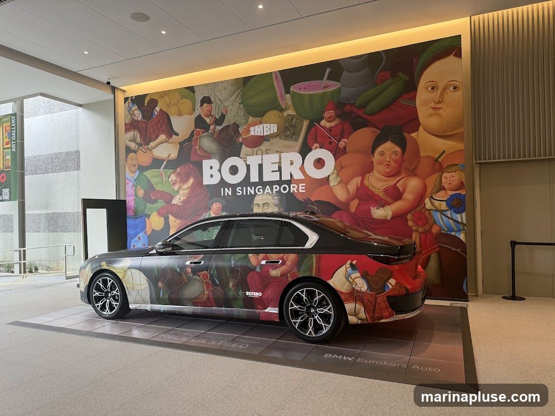 A black BMW sedan is displayed in front of a large mural featuring artwork by Fernando Botero. The mural depicts several of Botero's signature plump figures and still life elements. The car itself is also adorned with a wrap featuring Botero's artwork. The text "BOTERO in SINGAPORE" is prominently displayed on the mural. A banner for the "ART GALLERY" is visible to the left. The floor display includes text that reads "THE PRECIOUS STEED" and "BMW Eurokars Auto".
