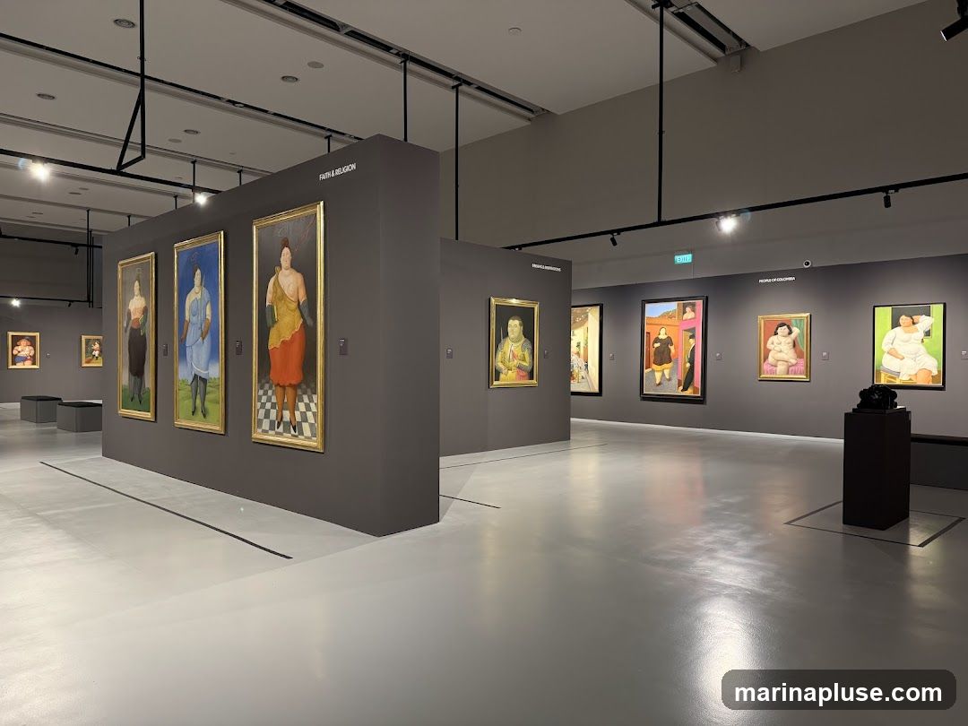 An art exhibition hall with several paintings displayed on grey walls. The paintings are portraits of people in various poses and attire. The hall has a polished grey floor and overhead lighting.