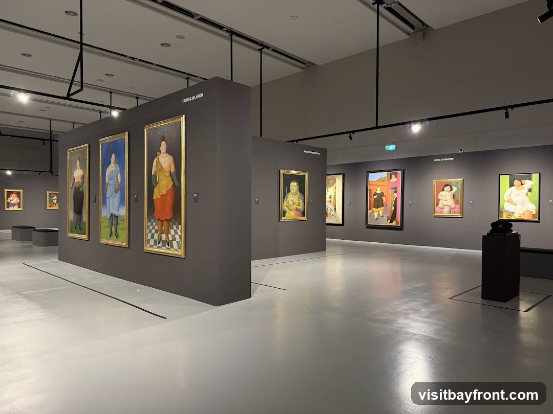 An art exhibition hall with several paintings displayed on grey walls. The paintings are portraits of people in various poses and attire. The hall has a polished grey floor and overhead lighting.