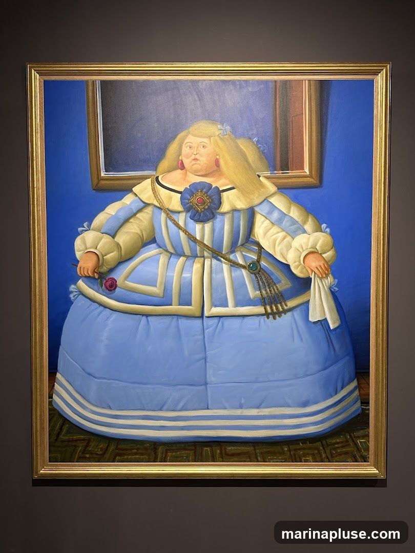 A painting in a gold frame depicts a woman with blonde hair and a full figure, wearing an elaborate blue and white dress. She has large pink earrings and a blue floral brooch with a red center. She holds a pink rose in her left hand and a white cloth in her right. The background is a solid blue wall with a framed dark rectangle. The floor has a patterned rug.