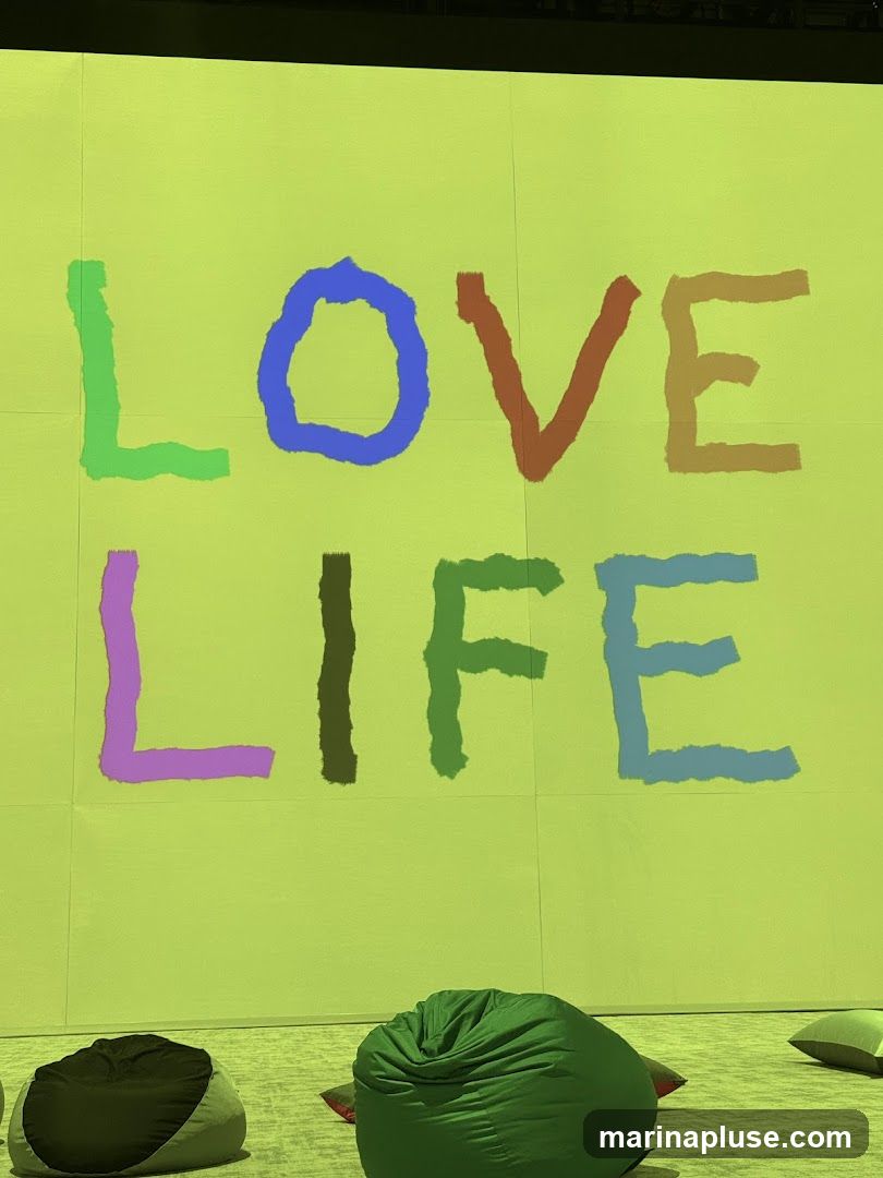 A bright lime green wall displays the words "LOVE LIFE" in large, colorful, hand-painted letters. Below the message, several beanbag chairs are scattered on the floor, suggesting a relaxed or communal space.