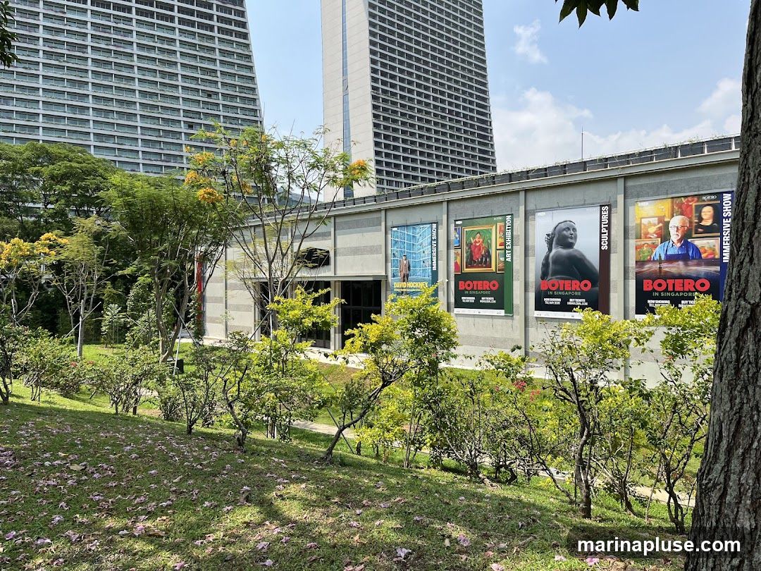 A row of large posters advertising art exhibitions is displayed on the exterior wall of a building. The posters feature artwork and text, including
