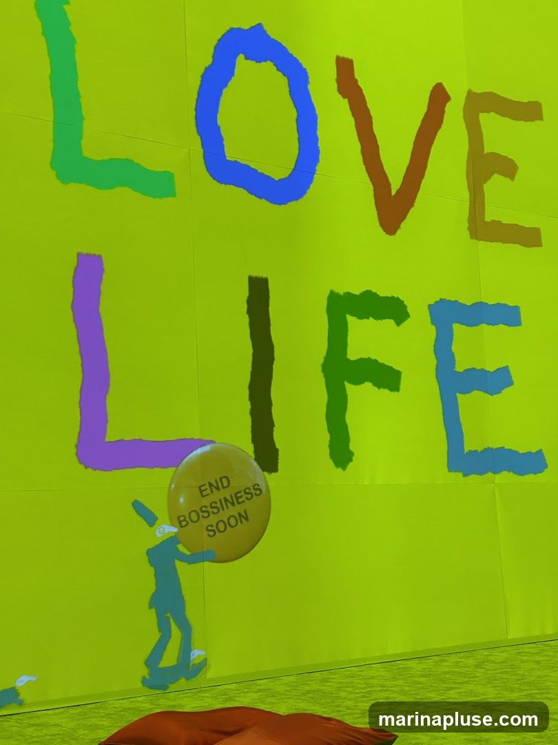 A bright green wall with the words "LOVE LIFE" painted in large, colorful, block letters. Below the text, a teal figure on a skateboard holds a yellow balloon that says "END BOSSINESS SOON". A red beanbag chair is visible in the foreground.