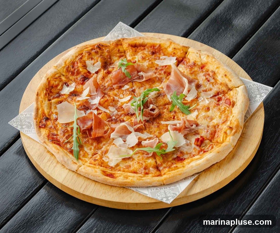 A close-up shot of a pizza topped with prosciutto, shaved parmesan cheese, and arugula, served on a wooden board with a branded paper liner. The pizza is on a dark wooden table.