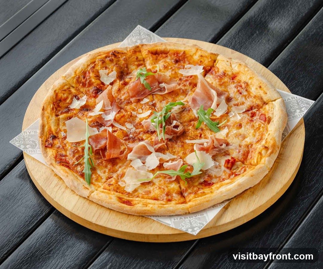A close-up shot of a pizza topped with prosciutto, shaved parmesan cheese, and arugula, served on a wooden board with a branded paper liner. The pizza is on a dark wooden table.