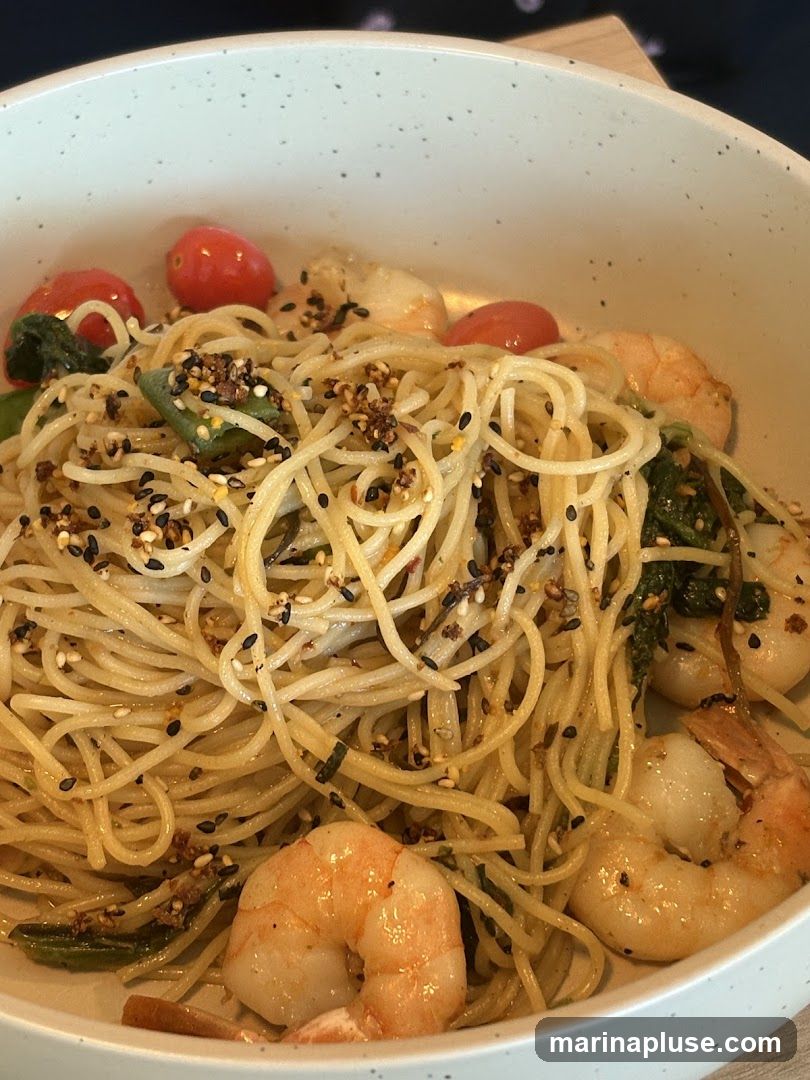 A close-up shot of a bowl of spaghetti with shrimp, cherry tomatoes, and greens, seasoned with sesame seeds and spices.