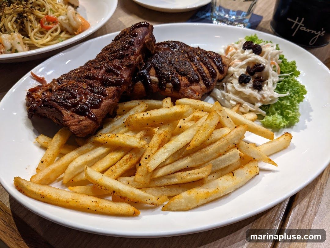 A plate of ribs and fries is served with a side of coleslaw. In the background, a plate of pasta with shrimp and a glass of water are visible. A dark container with the logo "Harry's" is also in the background.