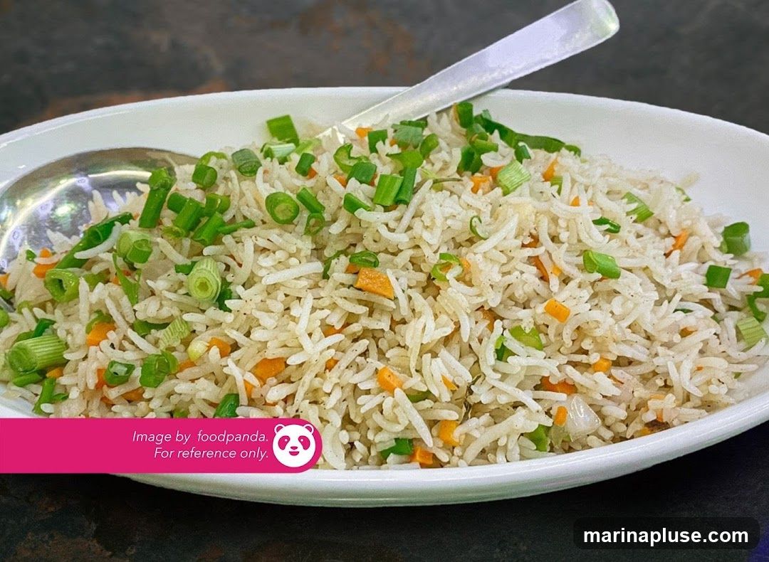 A close-up shot of fried rice in a white bowl, garnished with chopped green onions and diced carrots. A spoon is visible in the bowl. The image has a watermark that says "Image by foodpanda. For reference only."