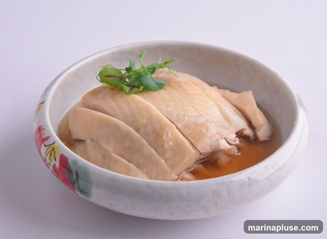 A bowl of sliced poached chicken served in a light broth, garnished with microgreens. The bowl has a decorative rim with floral patterns.