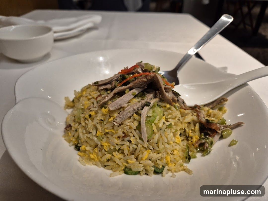 A close-up shot of a plate of duck fried rice, garnished with sliced red chili peppers and green herbs. The rice is mixed with scrambled eggs and vegetables. A spoon and fork are resting on the plate.