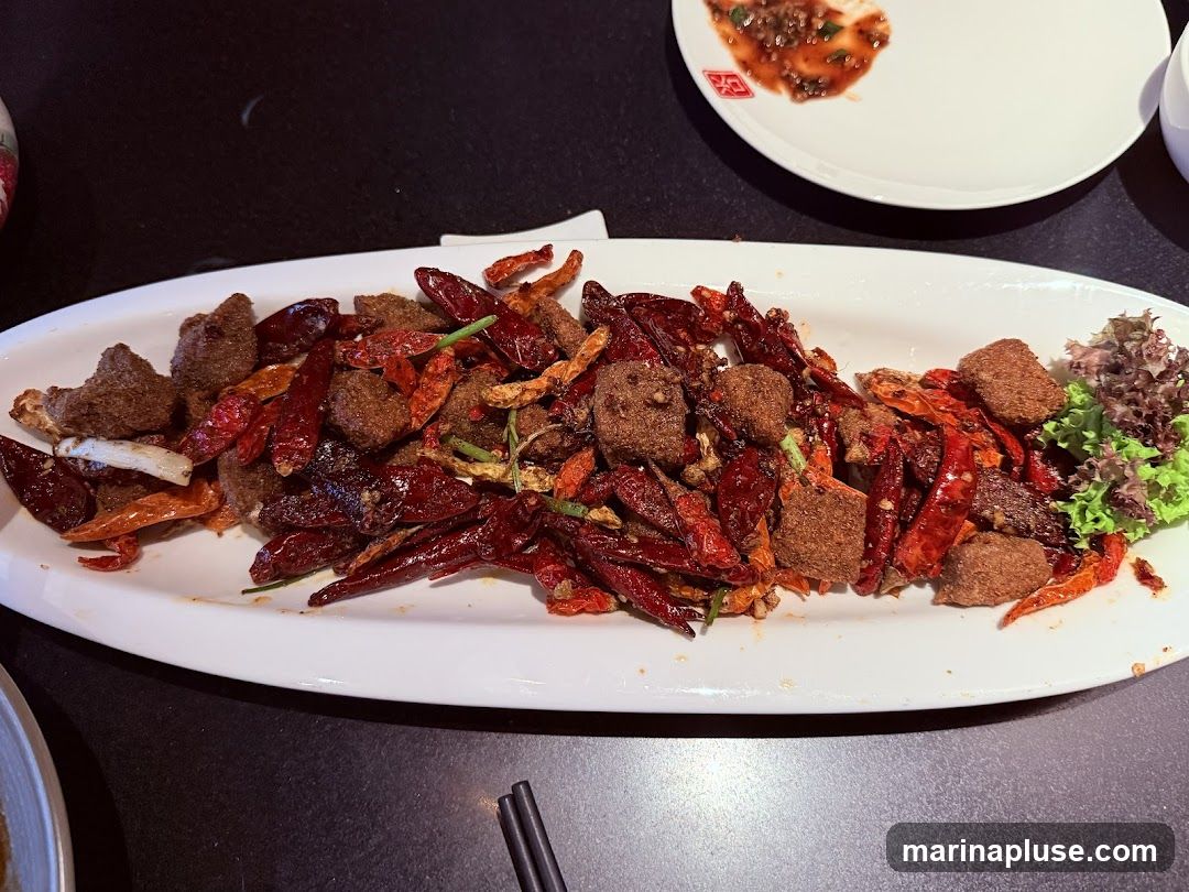 A white platter filled with bite-sized pieces of fried beef, mixed with a generous amount of dried red chilies and some green garnish. The dish appears to be seasoned with spices, giving it a textured, crumbly coating.