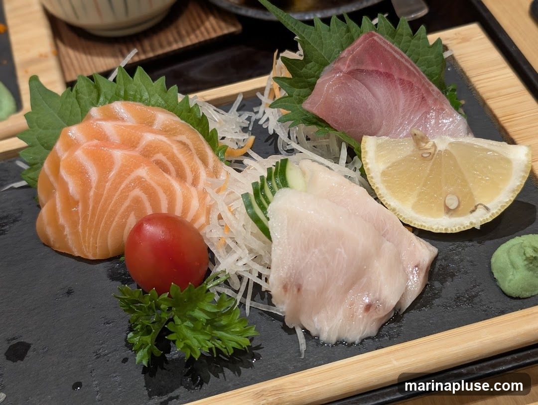 A close-up shot of a sashimi platter featuring slices of salmon, tuna, and white fish, garnished with shredded daikon, cucumber, a cherry tomato, parsley, a lemon wedge, and a dollop of wasabi.