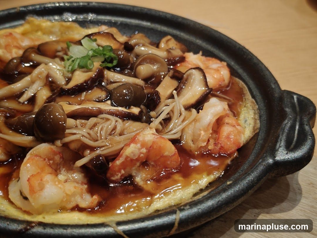 A close-up shot of a dish featuring shrimp and various mushrooms, including shiitake and enoki, in a savory sauce, served in a dark, textured bowl. The dish is garnished with chopped green onions.