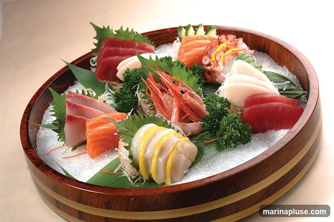 A wooden bowl filled with assorted sashimi, including tuna, salmon, hamachi, octopus, shrimp, and scallops, garnished with perilla leaves, shredded daikon, cucumber, and lemon slices, all resting on a bed of crushed ice.