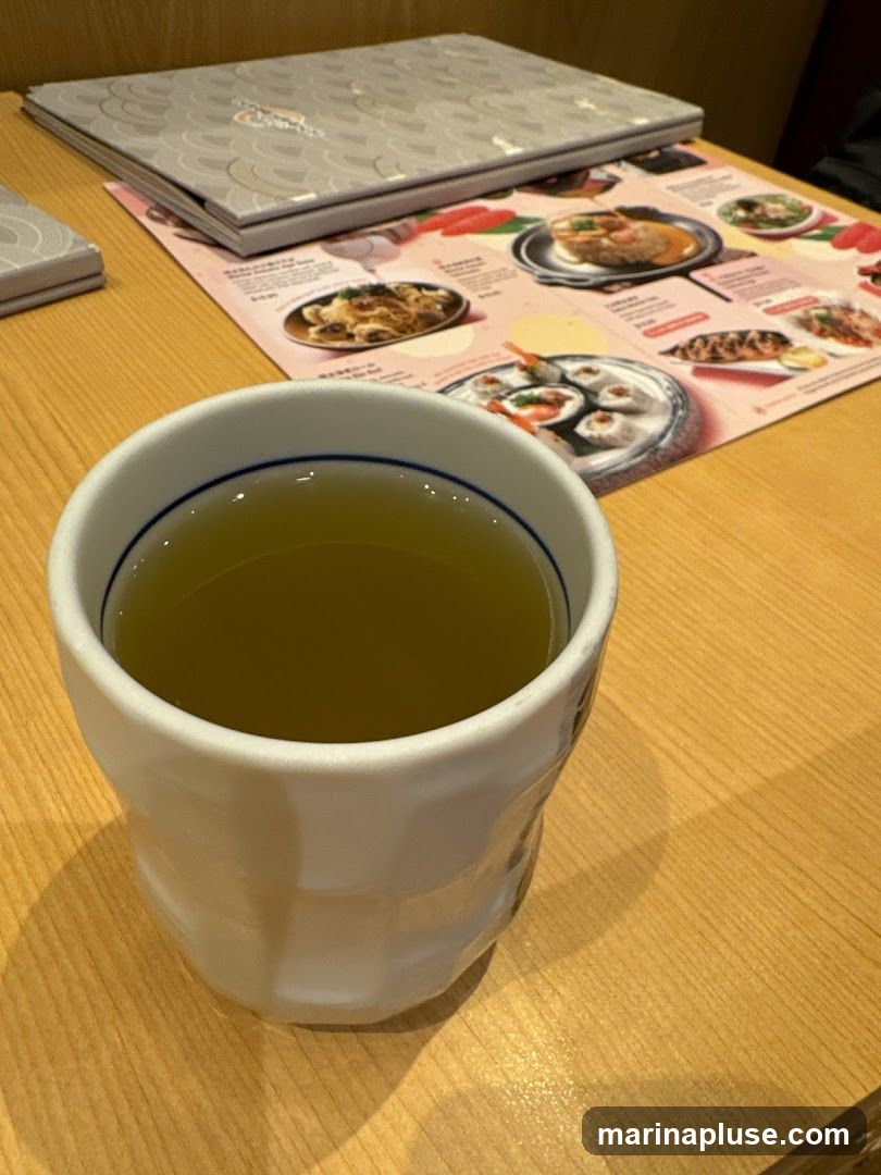A cup of green tea sits on a wooden table next to a menu with pictures of food.