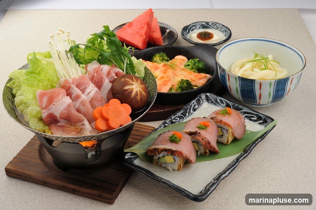 A spread of Japanese dishes including a hot pot with thinly sliced pork, napa cabbage, enoki mushrooms, and shiitake mushrooms. There is also a dish of salmon with broccoli, a small bowl of udon noodles, watermelon slices, and sushi rolls topped with what appears to be seared meat and roe.
