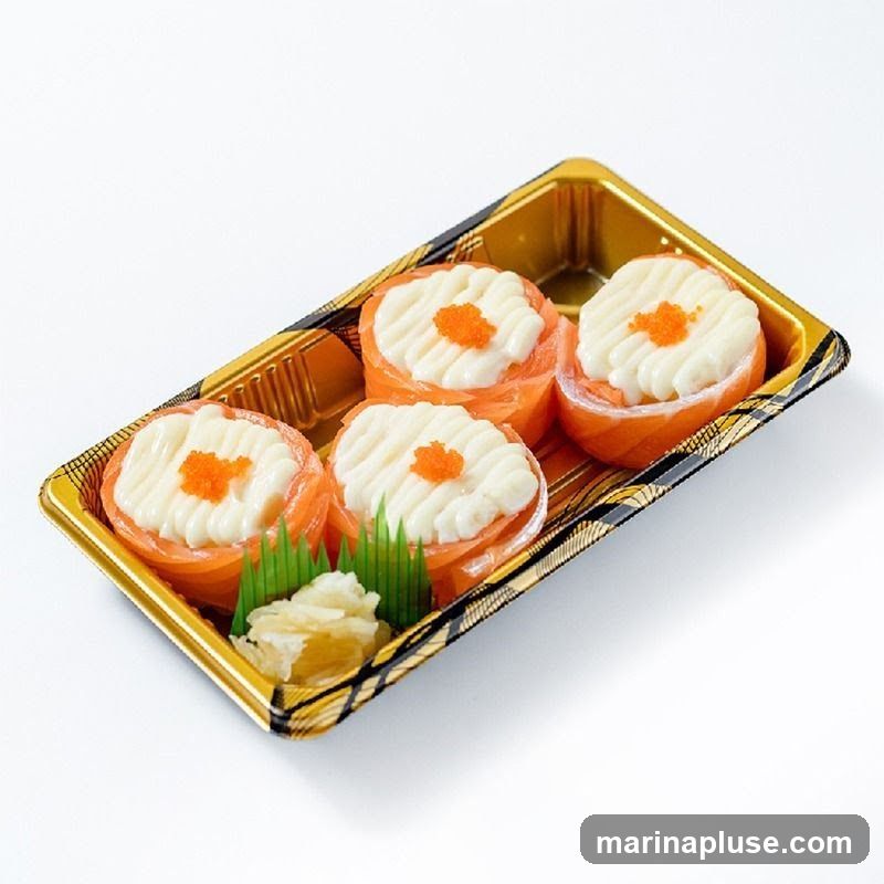 Four pieces of salmon sushi bites topped with white sauce and orange roe, served in a golden plastic container with pickled ginger and green garnish.