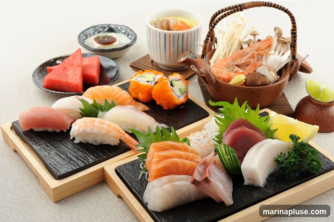 A close-up shot of a beautifully arranged platter of sushi and sashimi. The platter includes various types of nigiri sushi with salmon, tuna, and shrimp, as well as maki rolls covered in orange roe. Alongside the sushi are slices of sashimi, including salmon and tuna. A small dish of watermelon slices, a bowl of chawanmushi (savory egg custard), and a small pot with shrimp and mushrooms are also visible. The presentation is elegant, with garnishes of shiso leaves, parsley, lemon, and shredded daikon radish.