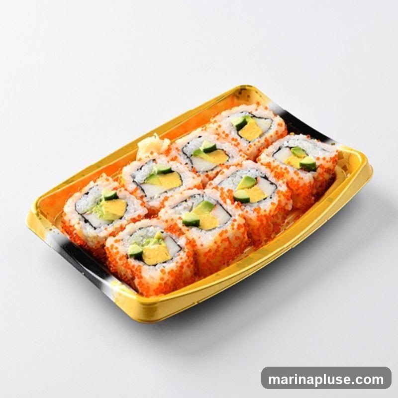 A tray of California rolls, also known as an inside-out roll, with rice on the outside coated in tobiko (flying fish roe), and filled with crab stick, avocado, and cucumber. A small portion of pickled ginger is visible on the side.