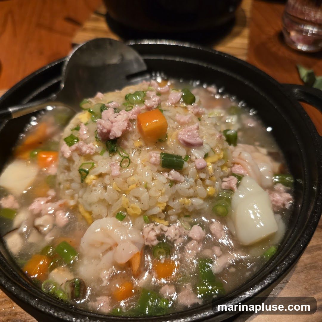 A close-up shot of a steaming bowl of fried rice topped with minced pork, shrimp, diced carrots, and green onions, all in a savory sauce. A serving spoon rests in the bowl.