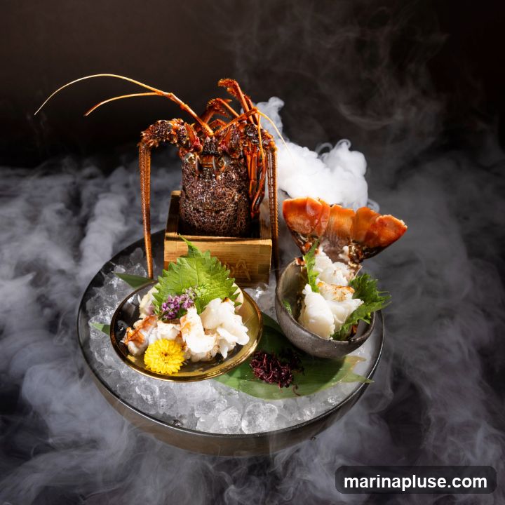 A whole lobster is presented on a bed of ice, with its tail and meat served separately in small dishes. The presentation is enhanced by wisps of smoke, creating a dramatic effect. The lobster meat is garnished with fresh green leaves and a small yellow flower.