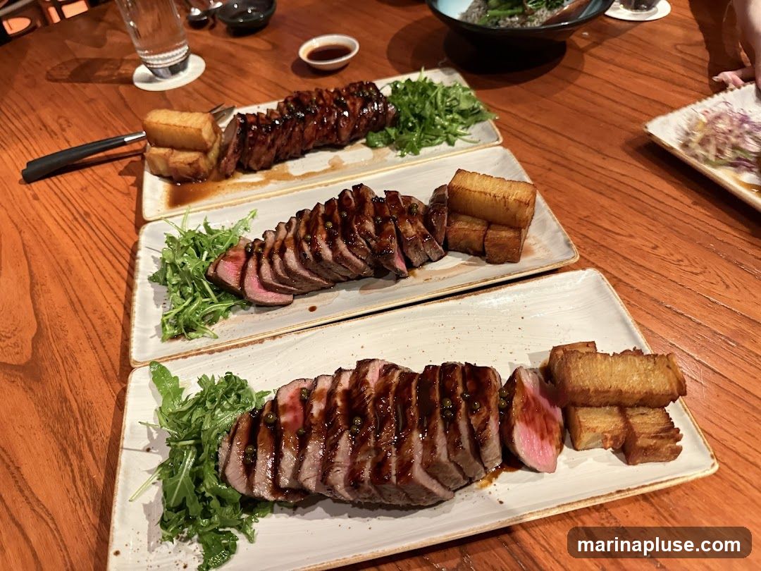 Three plates of sliced steak are arranged on a wooden table. Each plate features a portion of steak, some greens, and several pieces of fried potatoes. The steak is glazed with a dark sauce and some pieces have green peppercorns.