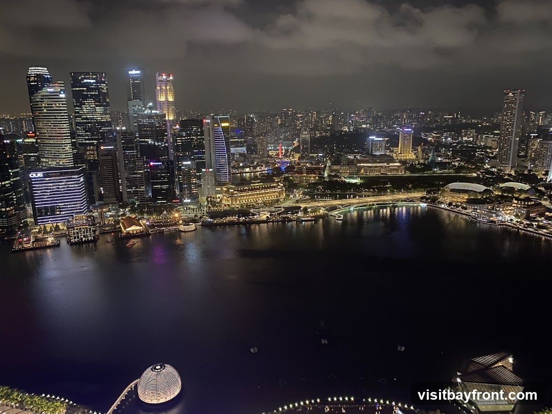 A panoramic view of the Singapore skyline at night, showcasing illuminated skyscrapers and the Marina Bay area. The water reflects the city lights, creating a vibrant and dynamic scene.