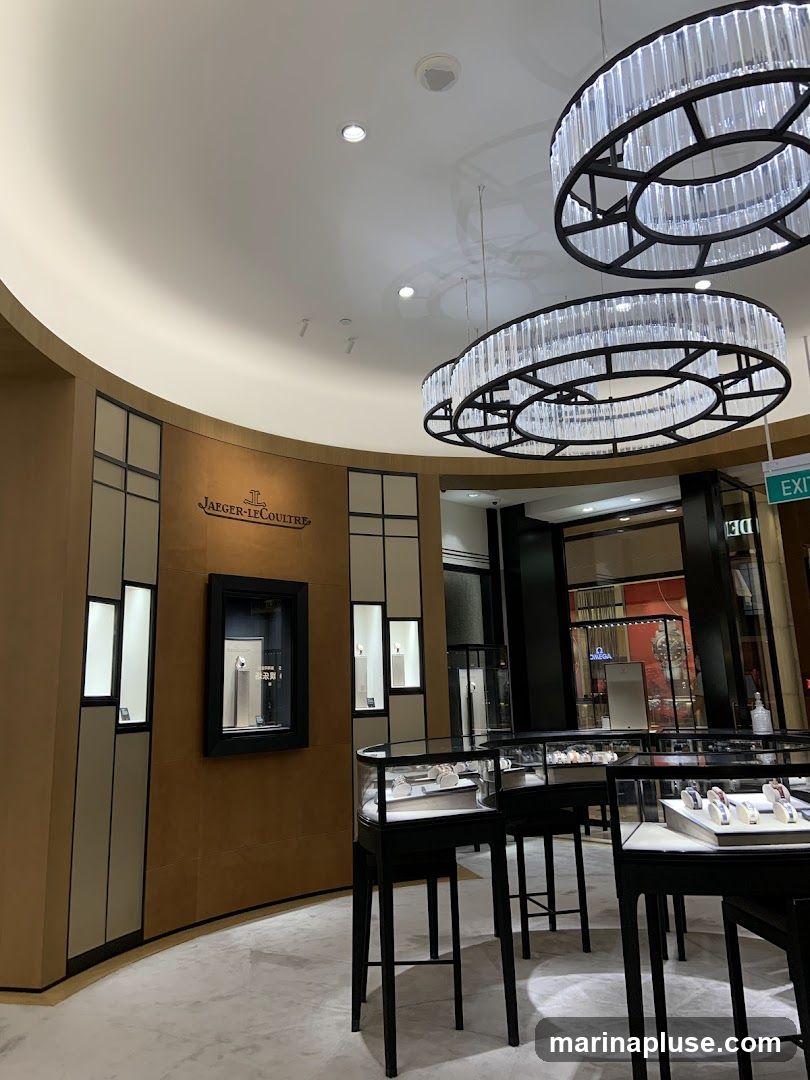 The interior of a luxury watch store, featuring display cases with watches and elegant chandeliers. The Jaeger-LeCoultre logo is visible on the wall.