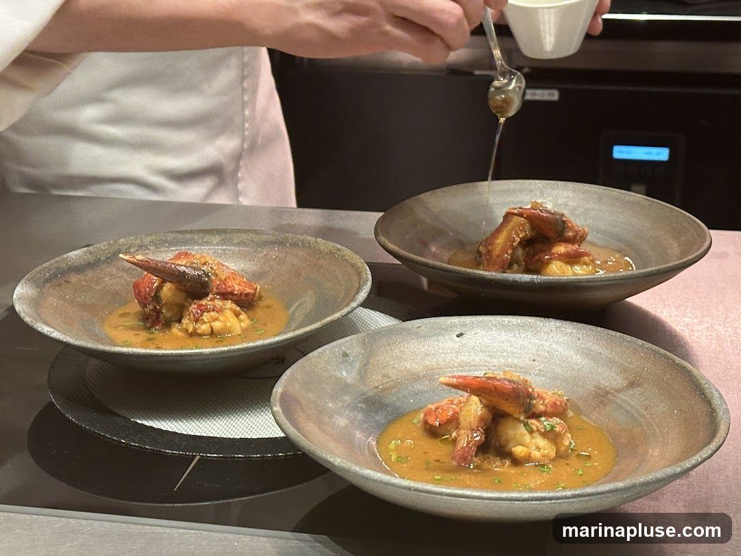 A chef in a white uniform is carefully drizzling a sauce over a beautifully plated lobster dish in a rustic bowl. The dish features succulent pieces of lobster in a rich, savory sauce, garnished with finely chopped herbs. Three bowls are visible, suggesting a multi-course meal or a shared appetizer. The background shows a professional kitchen setting.
