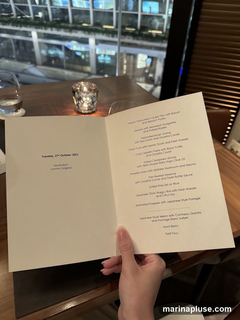A menu is held by a person's hand on a table in a restaurant. The menu lists various dishes and drinks.