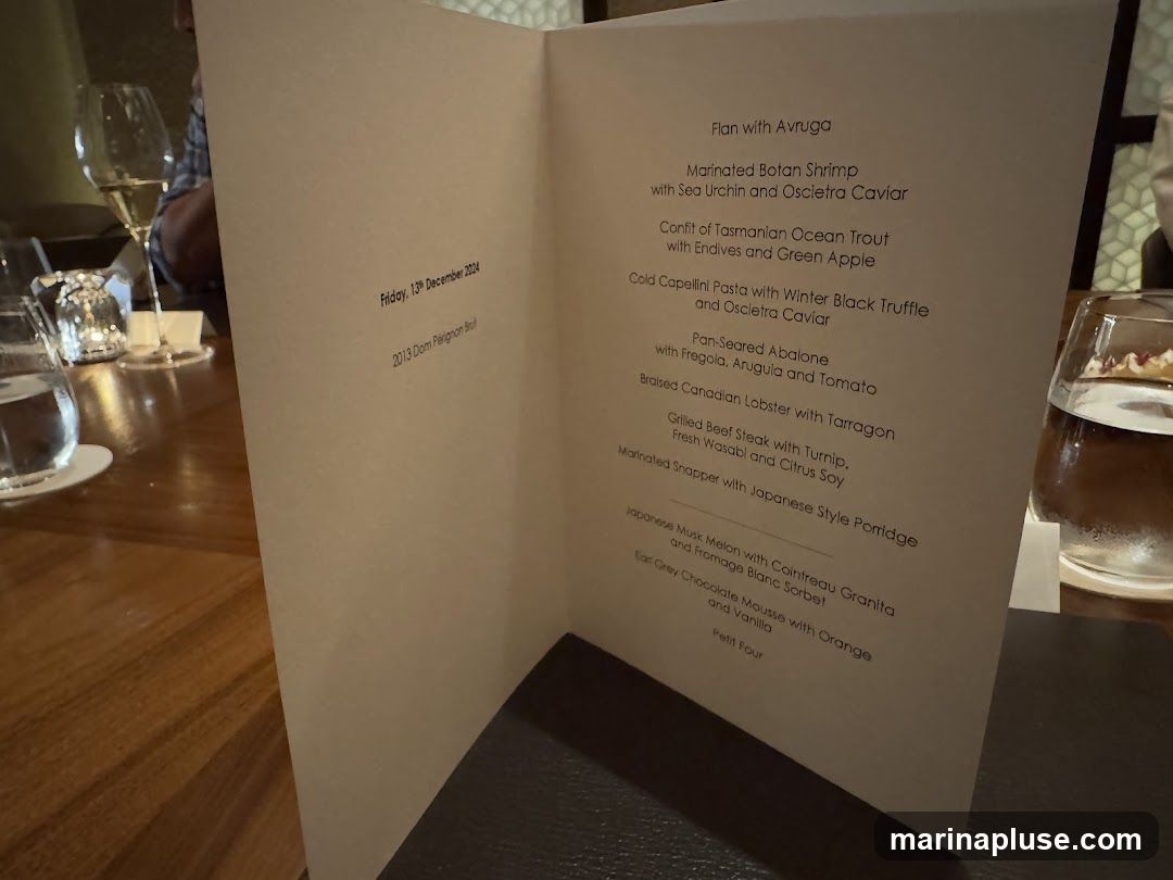 A menu is open on a wooden table, with a glass of champagne and a glass of water visible. The menu lists several dishes and a wine.