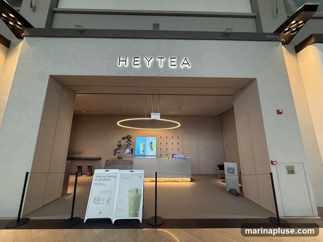 The exterior of a HEYTEA shop with the brand name illuminated above the entrance. Inside, a counter and display screens are visible. Two A-frame signs are placed outside the entrance, one announcing