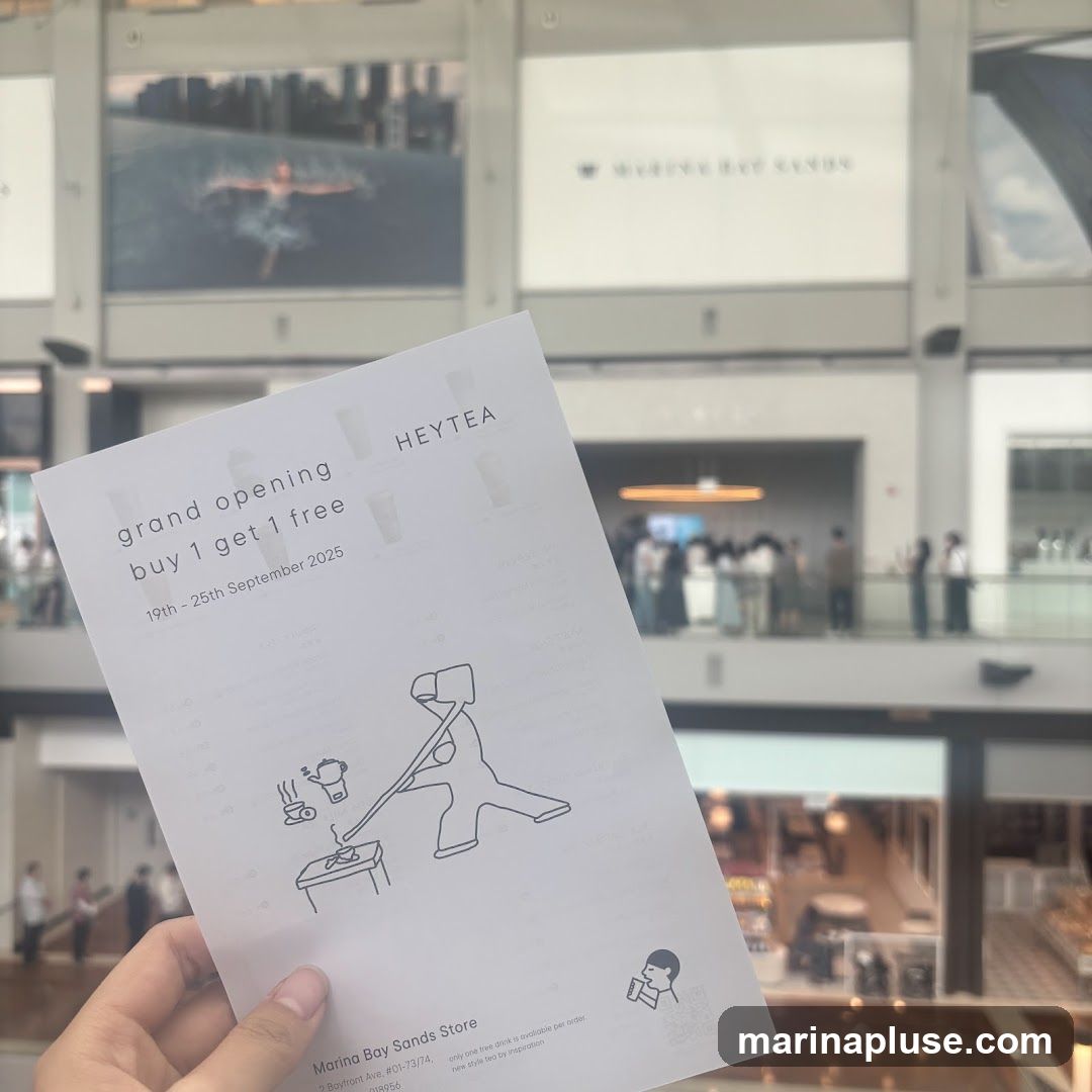 A flyer announcing the grand opening of HEYTEA with a buy 1 get 1 free promotion from September 19th to 25th, 2025. The flyer also includes the store's address at Marina Bay Sands and a tagline about new style tea. In the background, a blurred view of a shopping mall interior with people and store displays is visible.