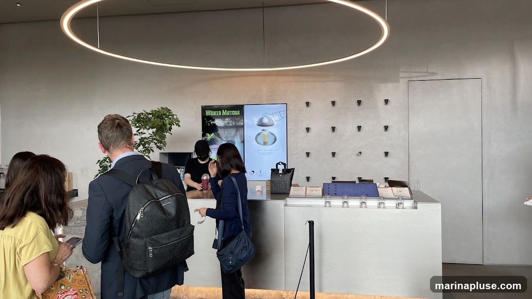 Customers are queuing at a counter in a modern matcha shop. A digital screen displays the shop's name,