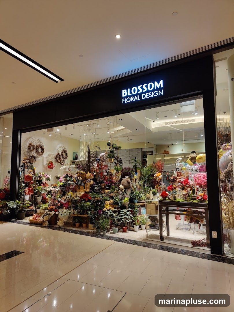 A well-lit storefront displaying a wide variety of flowers, plants, and teddy bears. The shop's name, "BLOSSOM FLORAL DESIGN," is prominently displayed on a sign above the entrance. The interior is filled with colorful floral arrangements, potted plants, and decorative items, creating a vibrant and inviting atmosphere.