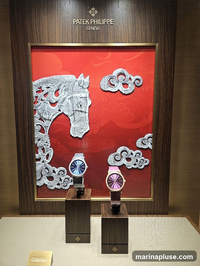 A display case featuring two Patek Philippe watches. The background is red with a decorative silver horse and clouds. The watches are presented on dark wooden stands. A small brass plaque reads "Calatrava". The Patek Philippe Geneve logo is visible above the display.