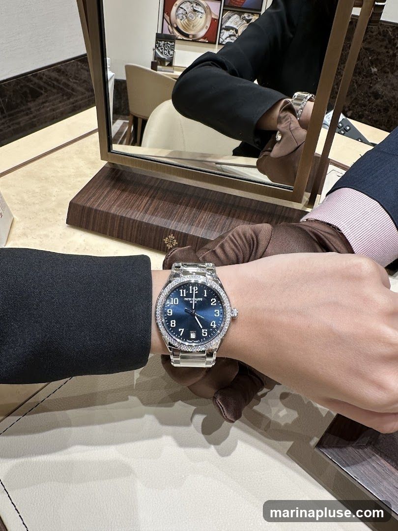 A person wearing a diamond-bezel watch with a blue dial is shown in a mirror reflection. The watch is on display in a store, with a salesperson wearing gloves assisting. The background shows other watches and store decor.