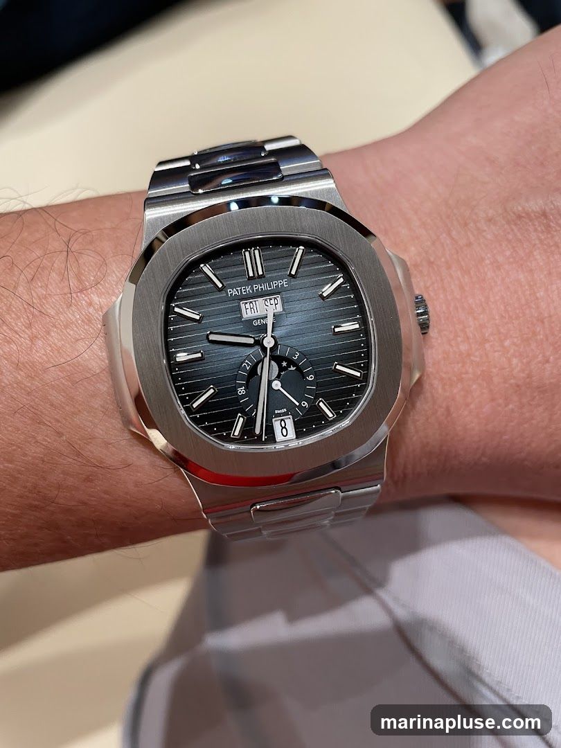 A close-up shot of a Patek Philippe Nautilus watch on a person's wrist. The watch has a dark blue dial with horizontal lines and silver hour markers. The date window shows '8' and the day is 'FRI SEP'. The watch has a stainless steel bracelet.