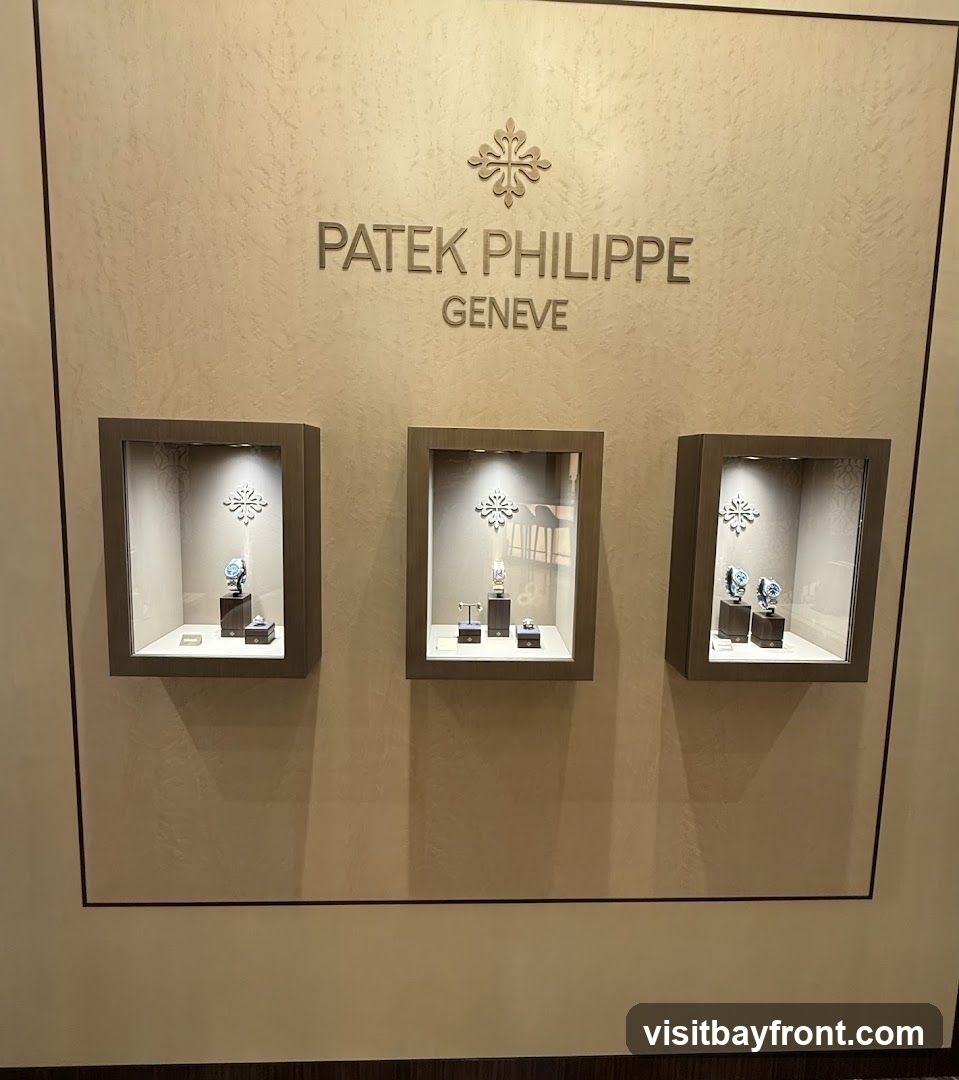 A wall display featuring the Patek Philippe Geneve logo and three illuminated display cases. Each case showcases watches on stands. The wall has a textured finish.