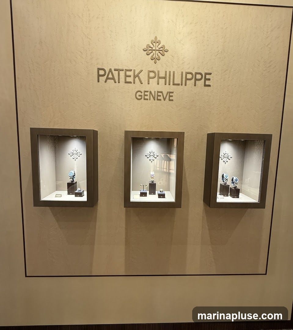 A wall display featuring the Patek Philippe Geneve logo and three illuminated display cases. Each case showcases watches on stands. The wall has a textured finish.