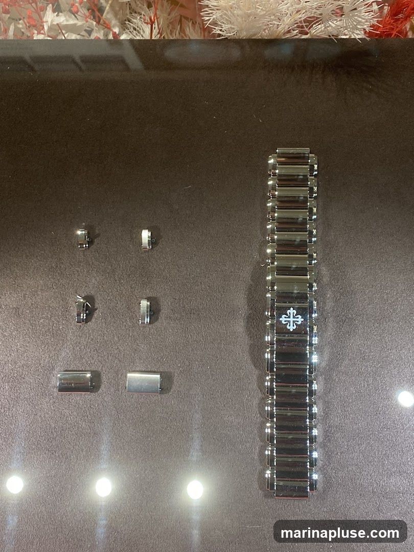 A display of watch bracelet components, including several individual links and a partial bracelet. The bracelet features a Patek Philippe logo.