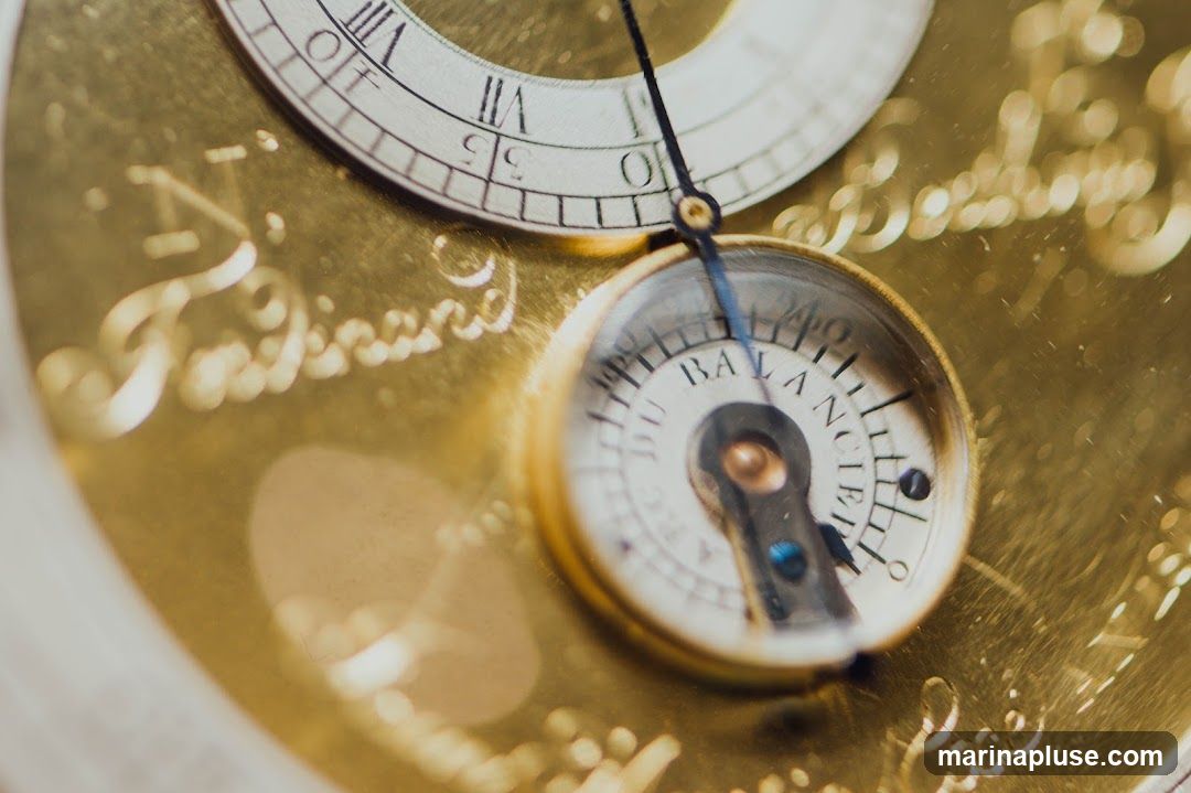 A detailed, close-up shot of the intricate workings of a vintage watch. The golden metal casing is engraved with elegant script, possibly a maker's name like 'Ferdinand'. A small dial, labeled 'BALANCE', is visible, along with Roman numerals on a larger dial in the background. The overall impression is one of craftsmanship and historical significance.